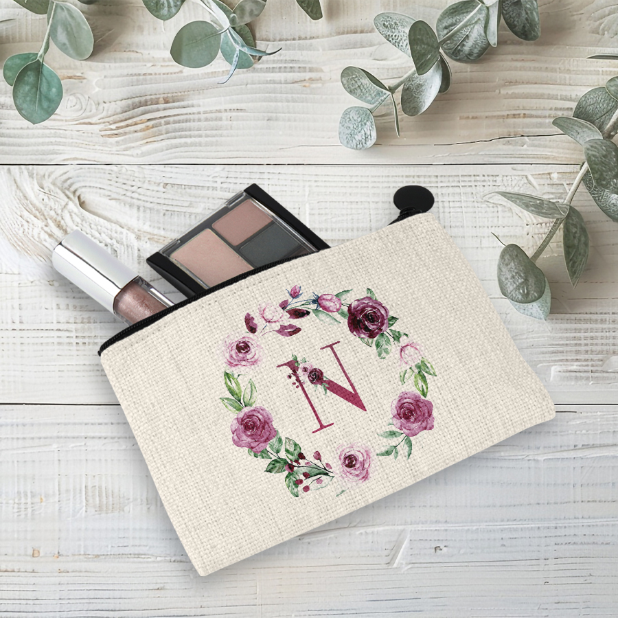 Linen coin purse featuring a pink rose wreath and initial with makeup in the bag.
